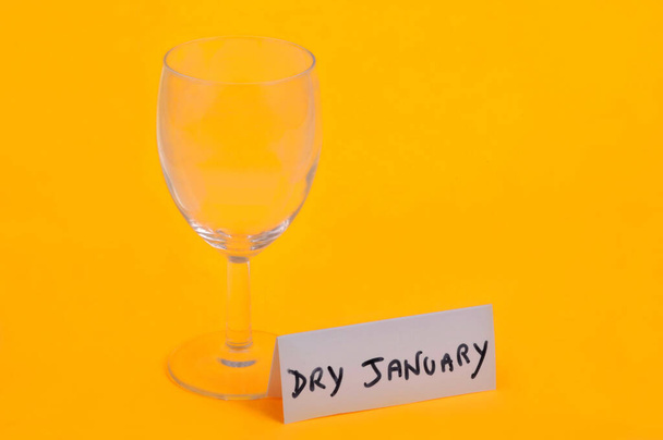 Droog januari concept met een leeg wijnglas en tekst op een kaart op een gele achtergrond - Foto, afbeelding