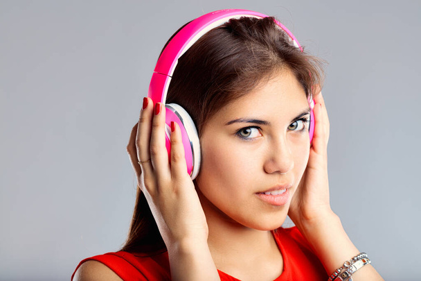 Encantada por el sonido, usa auriculares rosados, su expresión enfocada y relajada. Mujer joven con auriculares - Foto, imagen