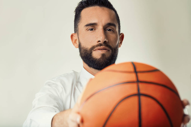 Profesyonel iş adamı, spor ve kurumsal stratejinin kesişimini gösteren bir basketbol topu tutuyor. - Fotoğraf, Görsel
