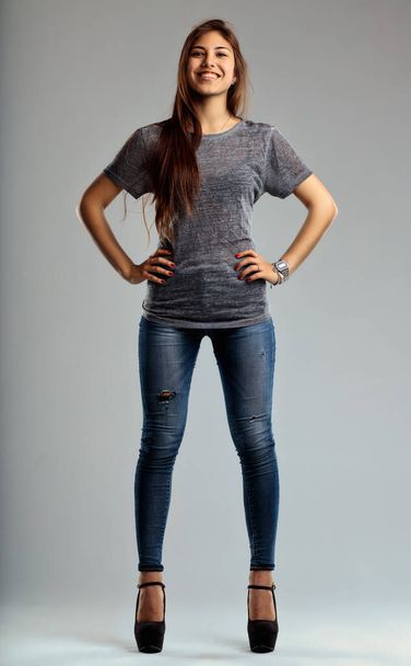 Νεαρή γυναίκα στέκεται με αυτοπεποίθηση σε στενά τζιν και τακούνια, το χαμόγελό της τόσο φωτεινό όσο το στυλ της - Φωτογραφία, εικόνα