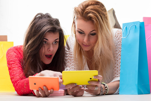Friends compare purchases and share excitement over a shopping spree, smartphones in hand - Photo, Image