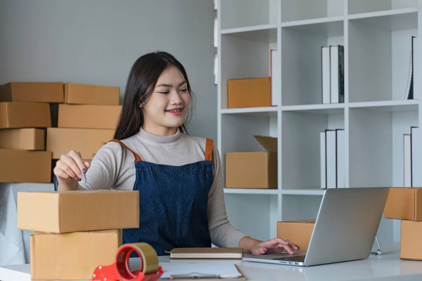 Startup SME small business entrepreneur SME or freelance Asian woman using a laptop with box, online marketing packaging box and delivery, SME concept.. - Photo, Image