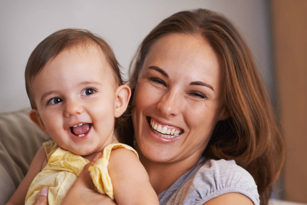 Mother, baby and smile in embrace at home, love and together for bonding in childhood. Mommy, daughter and support for happy toddler in child development, mama and security or connection on sofa. - Photo, Image
