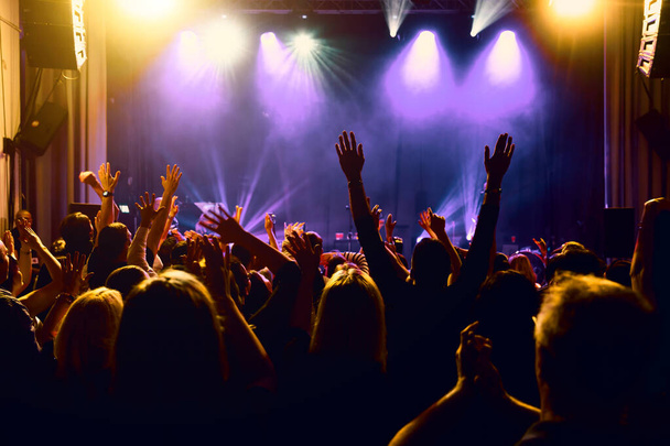 Multitud enérgica bajo vibrantes luces de escenario disfrutando de actuaciones de música en vivo. - Foto, Imagen
