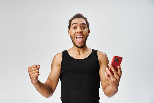 alegre deportivo afroamericano hombre sosteniendo el teléfono móvil y mirando a la cámara, apuestas en línea - Foto, Imagen