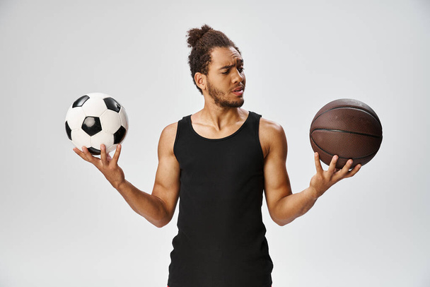 összezavarodott afro-amerikai sportoló pózol futball és kosárlabda kezében szürke háttér - Fotó, kép