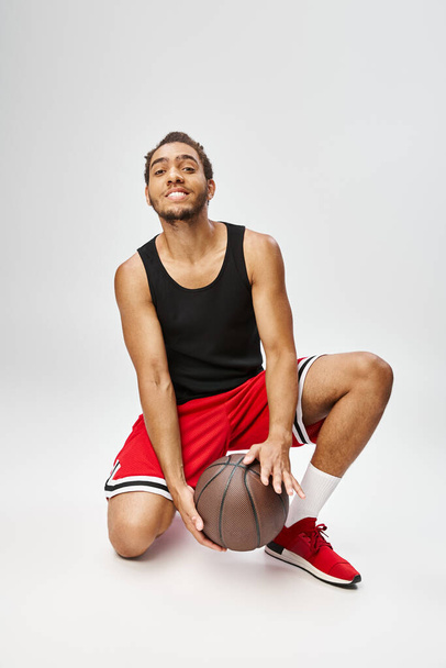 veselý africký Američan pózuje se svým basketbalem a usmívá se na kameru na šedém pozadí - Fotografie, Obrázek