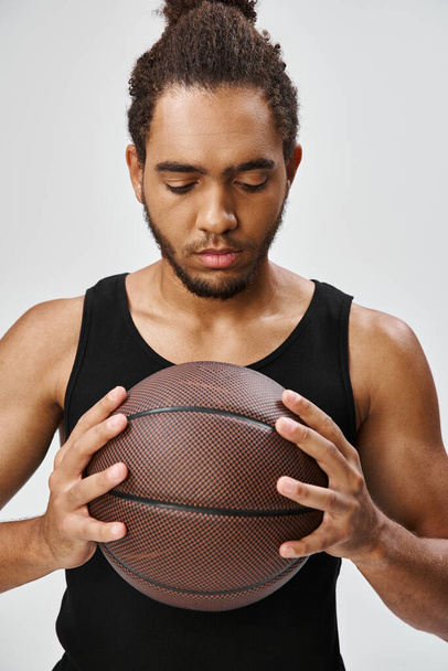 homme afro-américain attrayant dans un uniforme confortable posant avec son basket-ball dans les mains sur fond gris - Photo, image