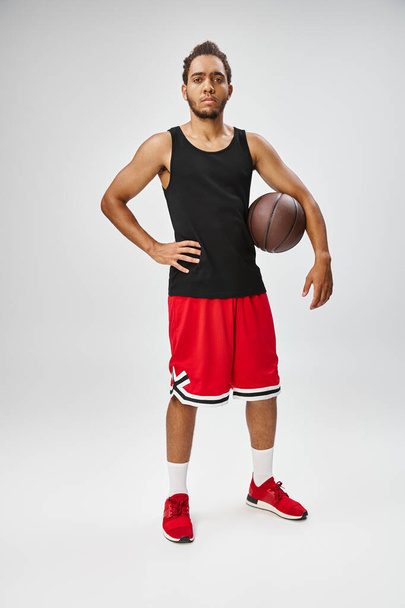 bell'uomo sportivo afroamericano che tiene il basket e guarda la macchina fotografica su sfondo grigio - Foto, immagini