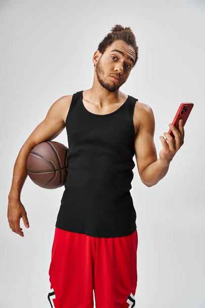 красивий афроамериканський чоловік тримає баскетбол і телефон і дивиться на камеру, онлайн ставки - Фото, зображення