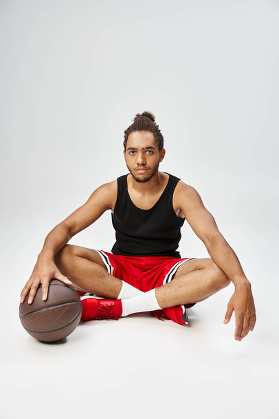bell'uomo afroamericano in abbigliamento sportivo seduto con le gambe incrociate sul pavimento con il basket - Foto, immagini