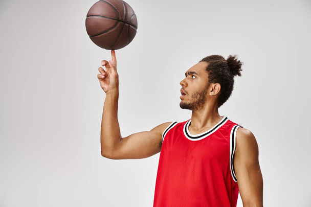 bien parecido atlético afroamericano hombre en ropa deportiva jugando baloncesto sobre fondo gris - Foto, Imagen