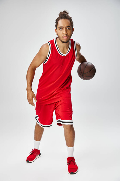 hombre afroamericano de buen aspecto sosteniendo el baloncesto y mirando a la cámara en el fondo gris - Foto, Imagen