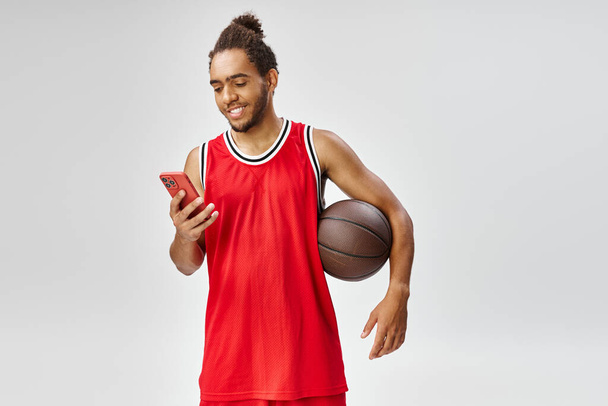 gioioso sportivo afro-americano in possesso di basket e guardando il suo smartphone, scommesse online - Foto, immagini