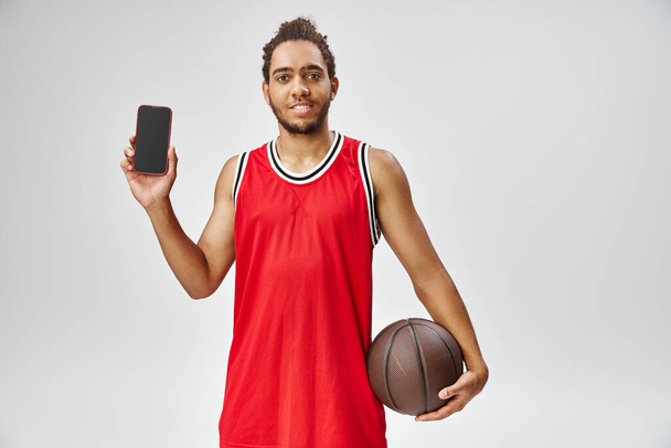 vidám sportos afro-amerikai férfi gazdaság kosárlabda és mosolyog a kamera, online fogadás - Fotó, kép