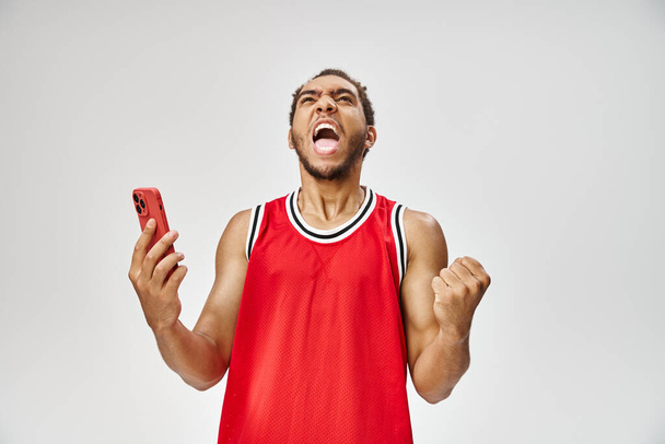 duygusal yakışıklı Afrikalı Amerikalı adam gri arka planda akıllı telefonu tutuyor, online bahis - Fotoğraf, Görsel