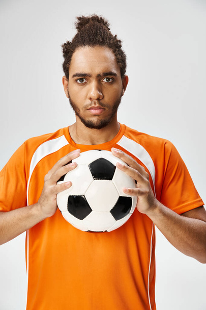 vonzó sportos afro-amerikai férfi pózol a futball és a kamera szürke háttér - Fotó, kép