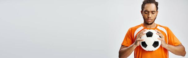 привлекательный атлетичный африканский американец в спортивной форме, смотрящий на футбол в руках, баннер - Фото, изображение