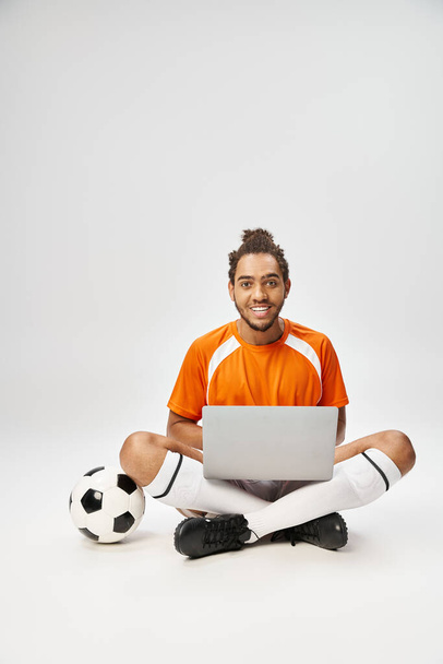 vreugdevolle Afrikaanse Amerikaanse sportman met voetbal en laptop op zoek naar camera, online wedden - Foto, afbeelding