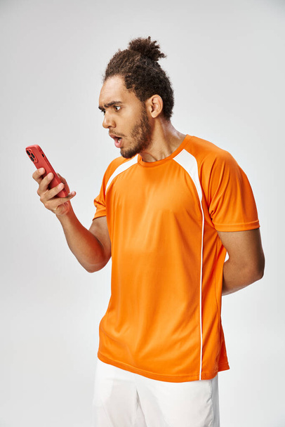 Şok olmuş Afrikalı Amerikalı sporcu gri arka planda akıllı telefonuna bakıyor, internette bahis oynuyor. - Fotoğraf, Görsel