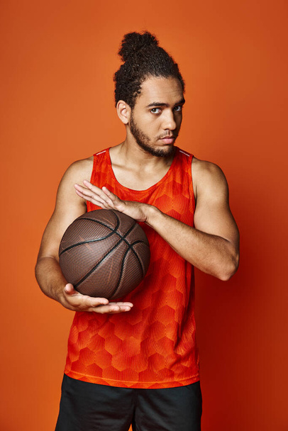 dobře vypadající atletický africký Američan ve sportovním oblečení drží basketbal a dívá se na kameru - Fotografie, Obrázek