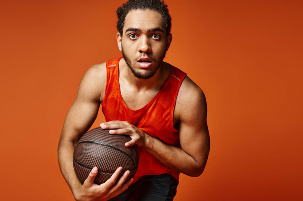 красивый африканский американец в спортивной форме активно играет в баскетбол и смотрит в камеру - Фото, изображение