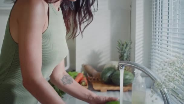 Zijaanzicht van jonge blanke vrouw wassen van groenten op gootsteen koken diner thuis - Video