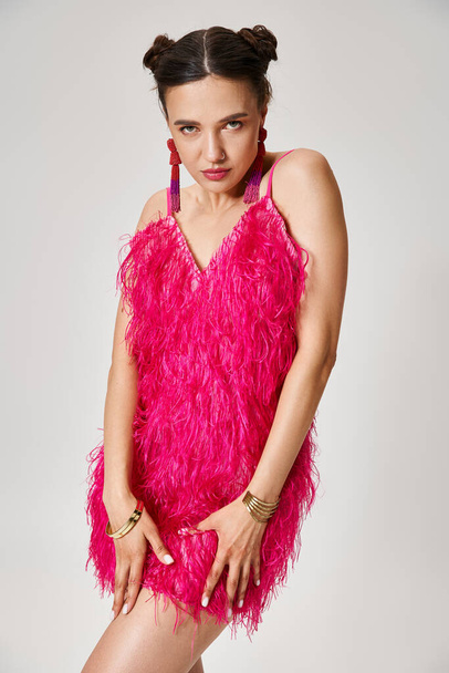 Radiant brunette woman in pink feather outfit holding her dress and looking to camera confidently - Photo, Image