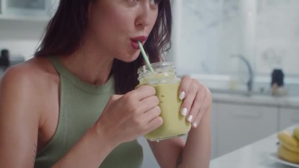 Tilt up shot van jonge vrolijke blanke vrouw drinken van groene appel en selderij smoothie met een gezond ontbijt thuis - Video