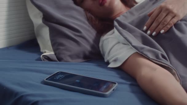 Colpo palmare di giovane donna che sente suonare l'allarme sul telefono cellulare e svegliarsi a letto - Filmati, video