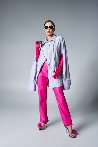 Стильна брюнетка в рожевих шкіряних штанях і модних сонцезахисних окулярах, що торкаються перлин на шиї - Фото, зображення