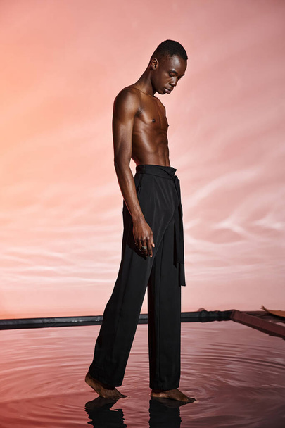 bell'aspetto uomo afroamericano senza maglietta che indossa pantaloni neri eleganti circondati da luci rosse - Foto, immagini