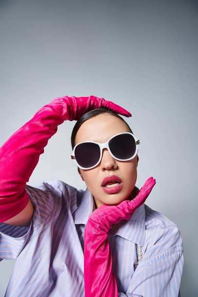 Fashionable woman with pink gloves elegantly touching her face, wearing sunglasses - Photo, Image