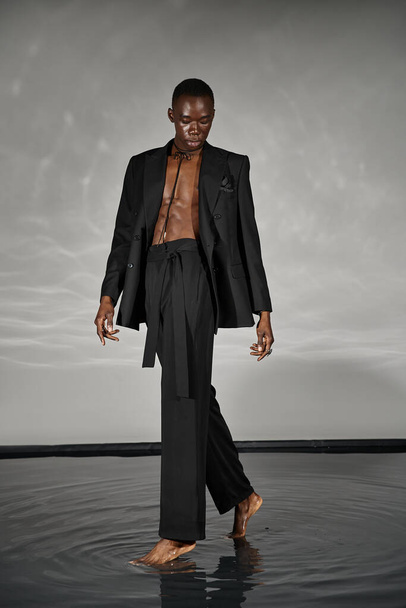 uroczy stylowy afrykański amerykański mężczyzna w sexy rozpięty garnitur pozowanie na szarym wodnistym tle - Zdjęcie, obraz