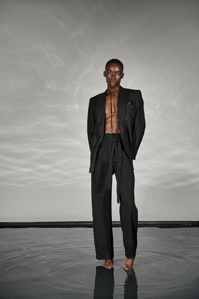 модний афроамериканський чоловік в чорному костюмі, який позує привабливо і дивиться на камеру - Фото, зображення