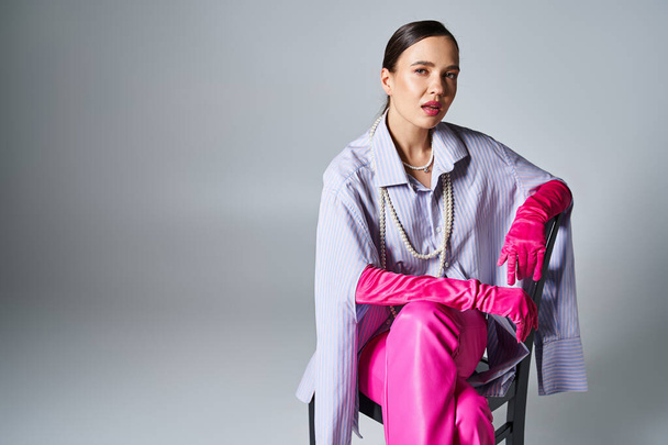 Confident brunette woman wearing pink gloves and stylish pants, sitting on chair - Photo, Image