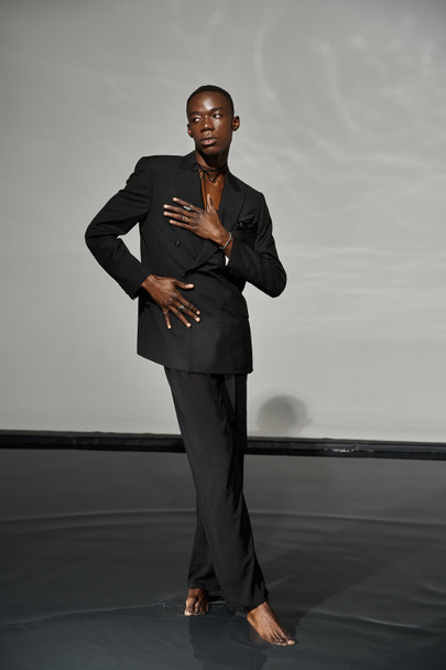 appealing stylish african american man in sexy unbuttoned suit posing on gray watery background - Photo, Image