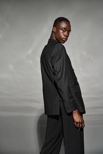 Afrikanisch-amerikanischer Mann im aufgeknöpften schwarzen Anzug posiert verführerisch und blickt in die Kamera - Foto, Bild