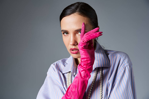 Fashionable woman with piercing in stylish outfit and pink gloves, covering her face with hand - Photo, Image