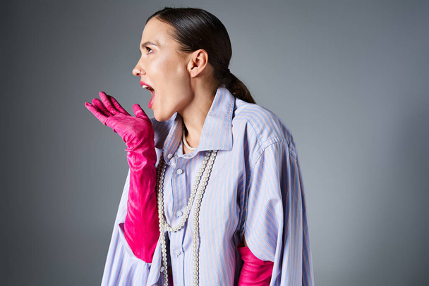 Modern woman with pink gloves, laughs joyfully with shouting while gesturing on grey backdrop - Photo, Image