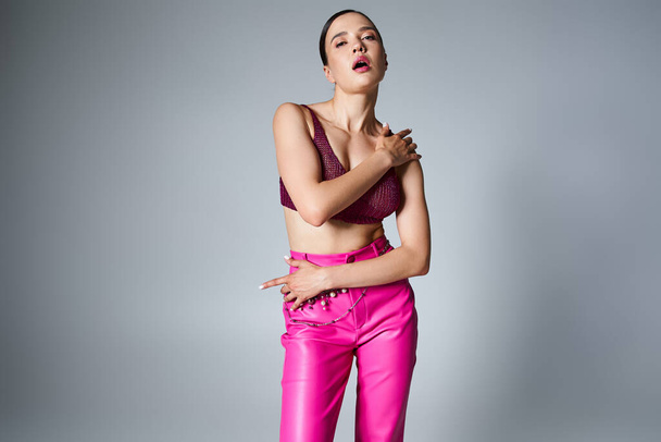 Modische Brünette in rosa Hose und dunkelrotem Oberteil, mit stylischem Schmuck, die Hände am Körper - Foto, Bild