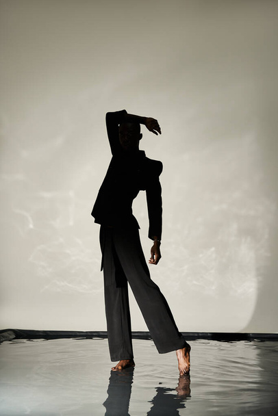 silueta stylového afrického Američana pózujícího bosý v obleku na vodnatém pozadí ve stínu - Fotografie, Obrázek