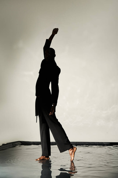 Силуэт модного африканского американца, позирующего босиком в костюме на сером водянистом фоне в тени - Фото, изображение