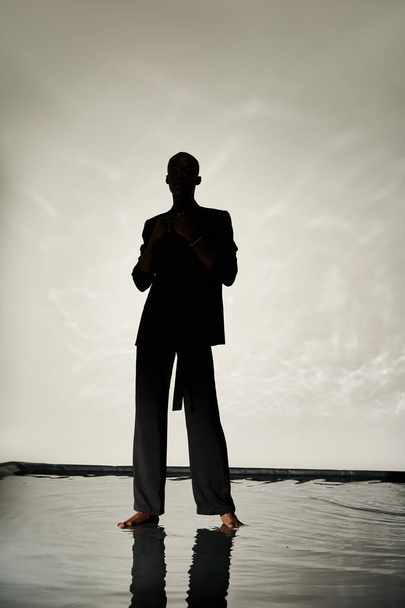 アフリカ系アメリカ人男性の魅力的なシルエットは,影の水面背景にスーツに裸足をポーズ - 写真・画像