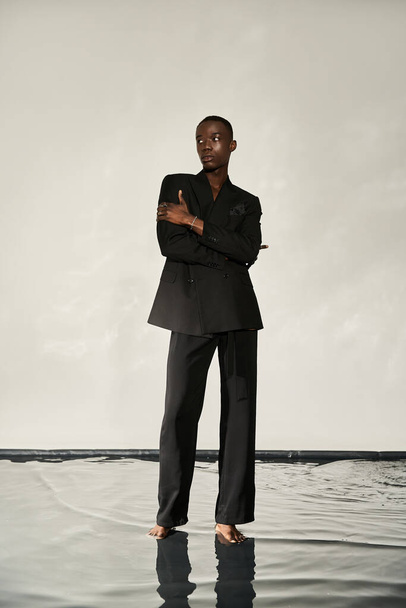 dobře vypadající africký Američan muž v elegantním černém obleku pózuje svůdně na vodnatém pozadí - Fotografie, Obrázek