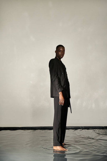 verführerisch afrikanisch-amerikanischer Mann im schwarzen sexy Anzug posiert attraktiv auf grauem wässrigem Hintergrund - Foto, Bild