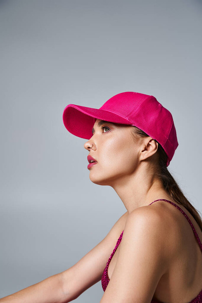 スタジオの設定でトレンディな服装とピンクの帽子で美しいブルネット女性の側面ビュー - 写真・画像