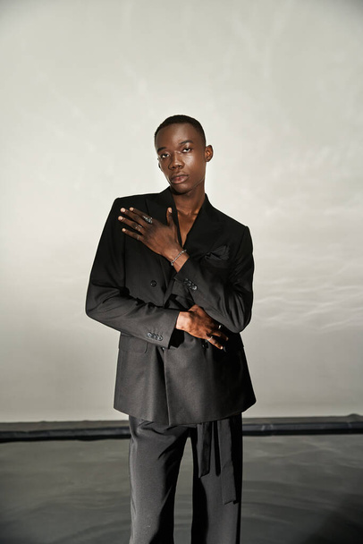 красивий афроамериканський чоловік в чорному сексуальному костюмі позує привабливо на сірому водному фоні - Фото, зображення