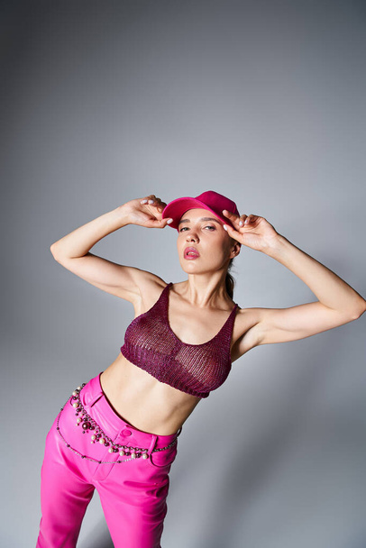 Fancy brunette woman in knitted top and pink trousers touching pink cap with one hand - Photo, Image