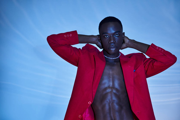schöner sexy afrikanisch-amerikanischer Mann in rotem, lebendigem Blazer, der in die Kamera auf blauem wässrigem Hintergrund blickt - Foto, Bild